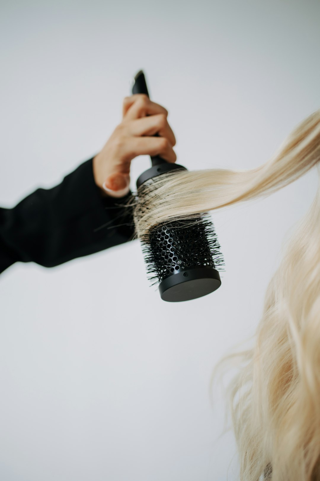 A hand using a round brush to style long blonde hair