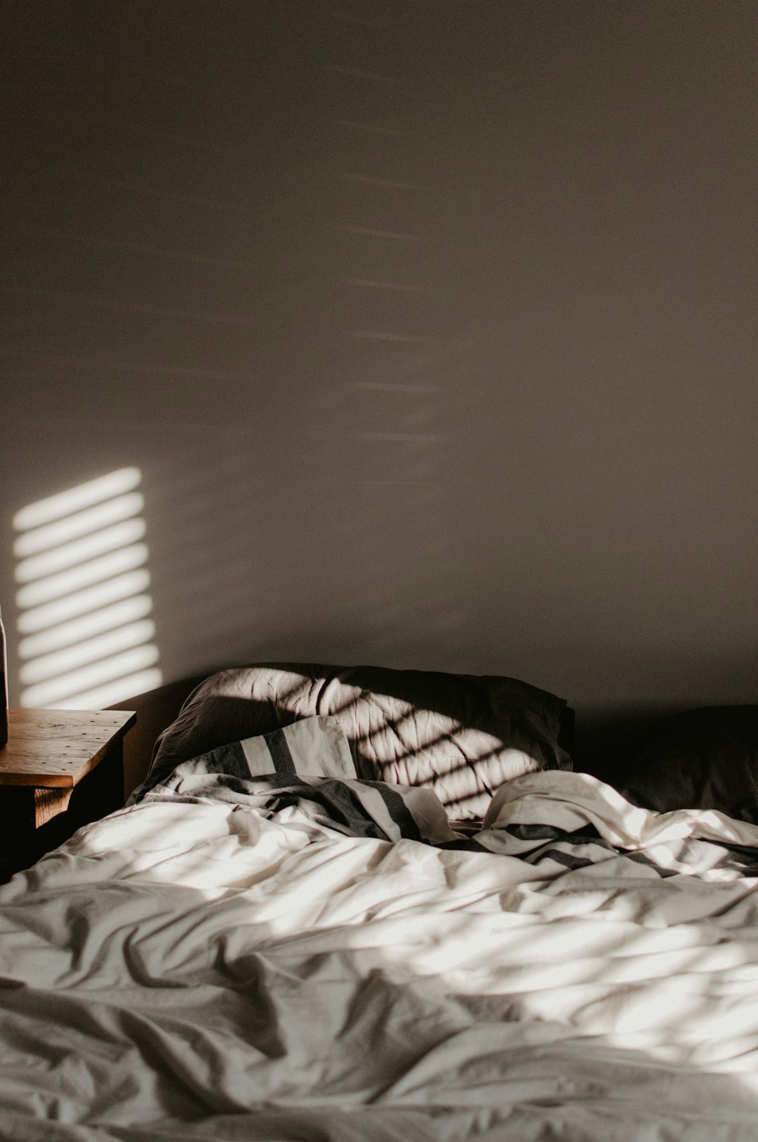 A rumpled bed with striped bedding in a room with slatted light patterns
