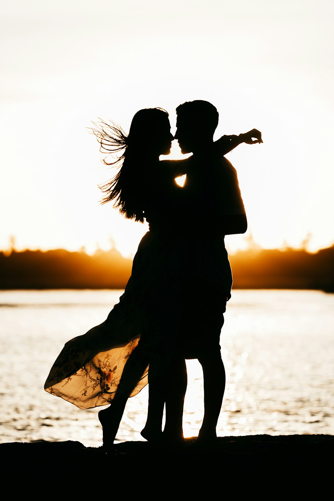 A silhouette of two people embracing against a bright golden light over water