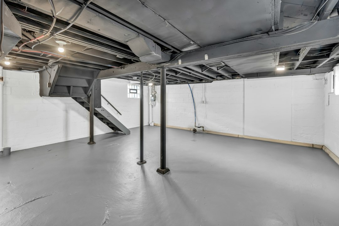 Spacious unfinished basement with exposed joists, support poles, and stairs